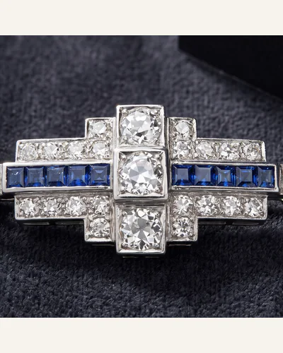 An Art Deco platinum brooch set with old-cut diamonds and calibré-cut sapphires, on charcoal velvet. — the centre stone.