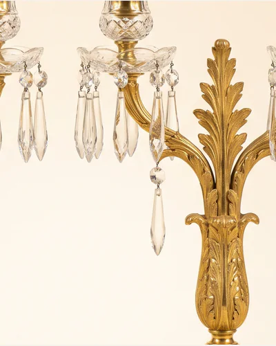 A pair of Regency ormolu and cut-glass candelabra hung with lustre drops, photographed on a warm paper plate. — gilding.