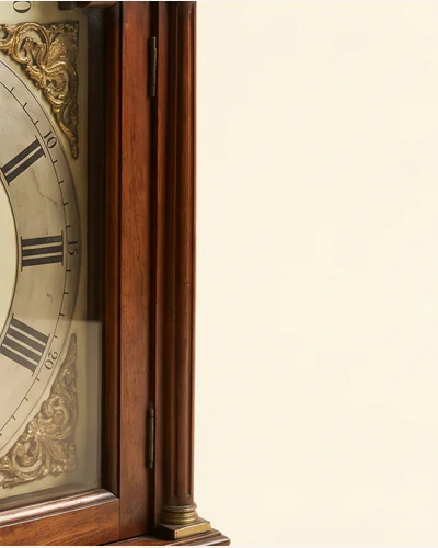 An eighteenth-century longcase clock hood with a painted arched dial and brass spandrels. — the spandrels.