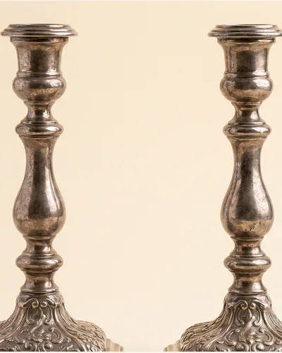 A pair of cast silver candlesticks with knopped stems and shaped square bases, on a warm paper plate.