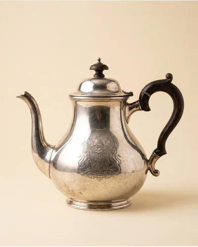 A Georgian sterling silver teapot with a fruitwood handle on a paper plate.