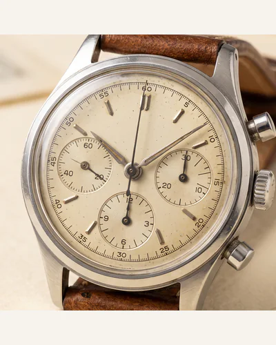 A vintage stainless steel chronograph wristwatch on a worn leather strap, photographed on a paper plate. — the dial.